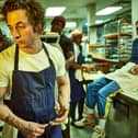 Jeremy Allen White as Carmen ‘Carmy’ Berzatto in The Bear, wearing a blue apron, holdin a spoon in a restaurant kitchen (Credit: Frank Ockenfels/FX )