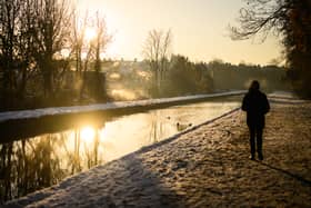 A man walks on the snow-covered path by the New River at sunrise, as steam rises from nearby houses in London.