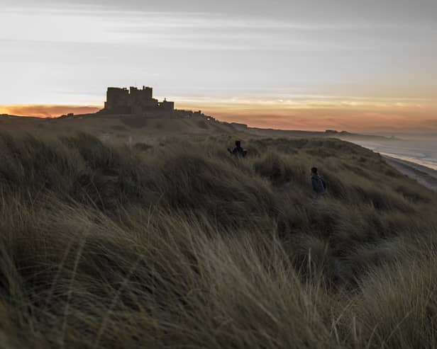 Children run through the sand dunes as the sun sets behind Bamburgh Castle