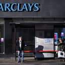 Commuters wait at a bus stop outside a branch of Barclays in London.