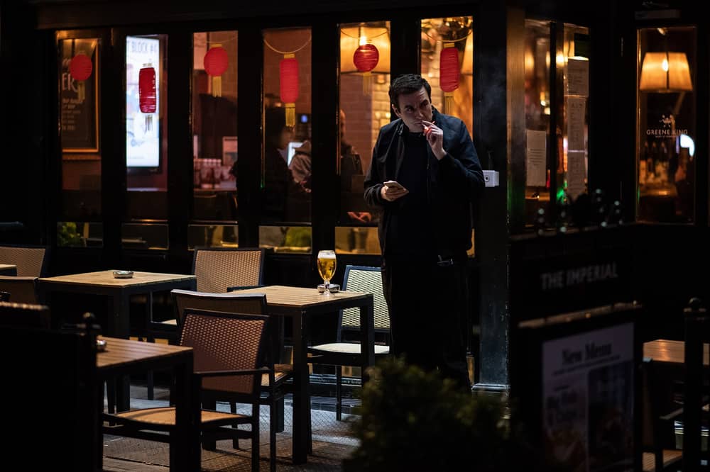 Man smokes a cigarette outside pub.