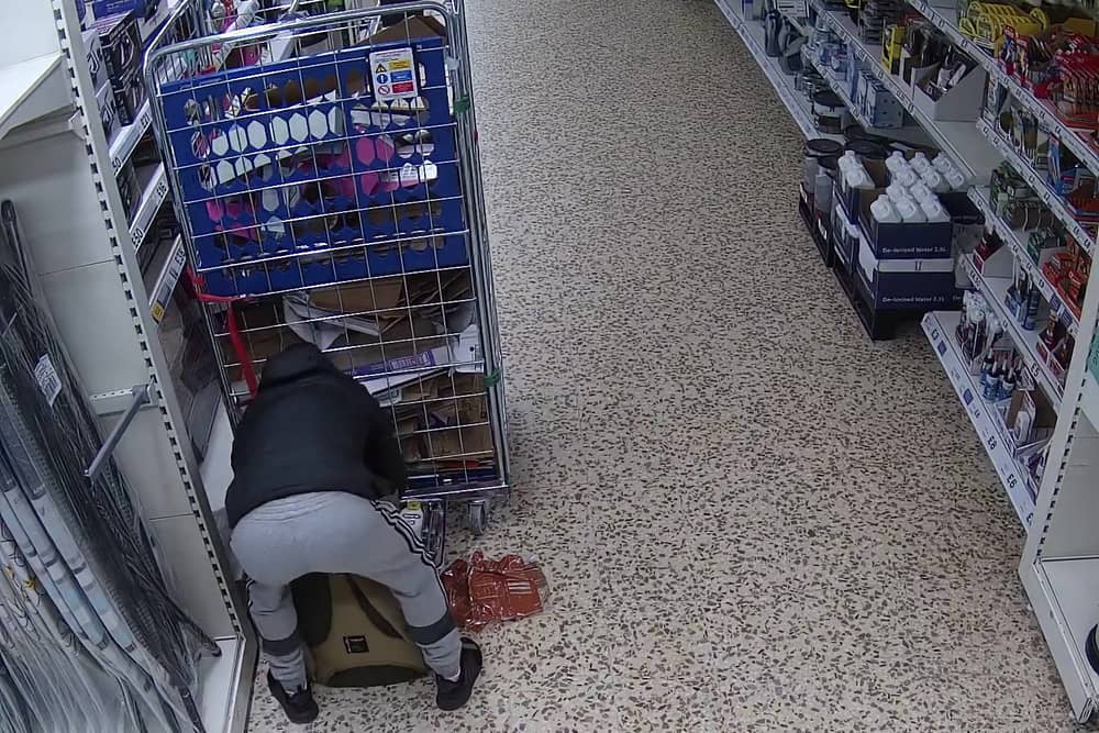 Video grab of Nicolae Boia crouched behind a trolley and filling his bag with unpaid for goods.