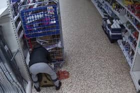 Video grab of Nicolae Boia crouched behind a trolley and filling his bag with unpaid for goods.