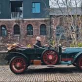 An antique car driving down a cobbled street