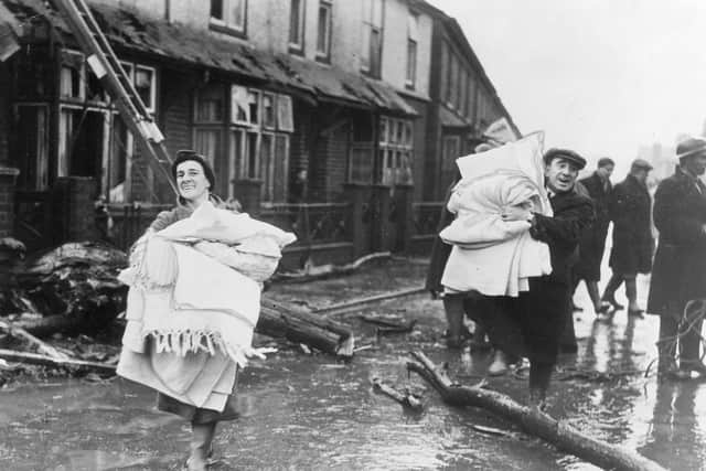 Resilient residents carry their belongings down mud-covered Brook Street, past fragments of the shattered tree. EMN-200211-181751001