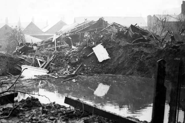 Damaged vehicles line the large crater where the 1,000kg German bomb fell in the Scalford Brook in Melton in November 1940. The collapsed GPO garage is visible behind. EMN-200211-181708001