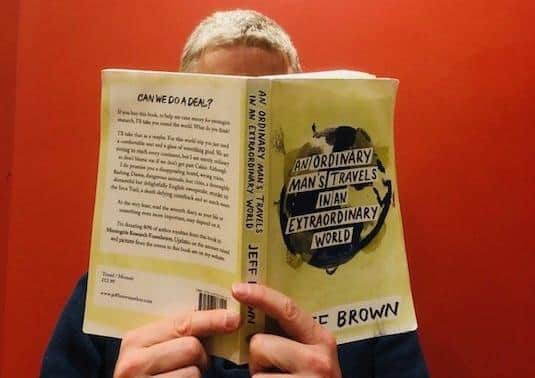 Jeff Brown behind a copy of his fundraising travel book EMN-200112-114744001