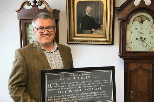 Ben Shouler, managing partner at Shouler and Son, in front of a photo of his great-great-great grandfather, William, who founded the company, and a framed announcement of the original formation of the business EMN-211207-182918001
