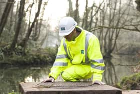 A Severn Trent employee inspects a drain near a river