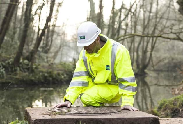 A Severn Trent employee inspects a drain near a river