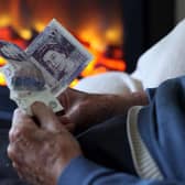 An elderly man holds cash in his hands as he warms himself in front of a fire - thousands of Melton borough pensioners will now lose winter fuel payments this year(Photo by Matt Cardy/Getty Images)