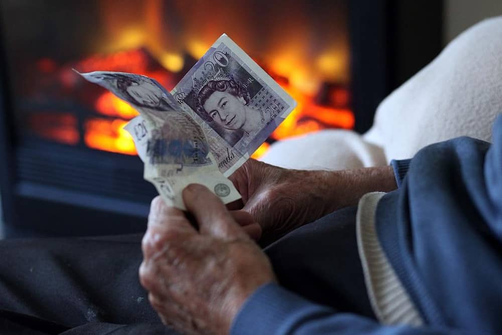 An elderly man holds cash in his hands as he warms himself in front of a fire - thousands of Melton borough pensioners will now lose winter fuel payments this year(Photo by Matt Cardy/Getty Images)