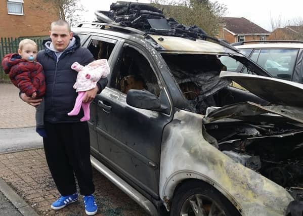 James Nairn, holding two of his young children, next to his car which was destroyed in an arson attack in Drummond Walk, Melton EMN-190402-141431001