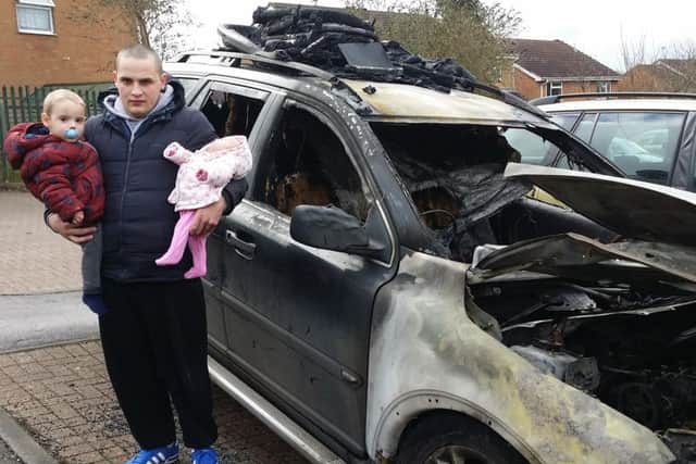 James Nairn, holding two of his young children, next to his car which was destroyed in an arson attack in Drummond Walk, Melton EMN-190402-141431001