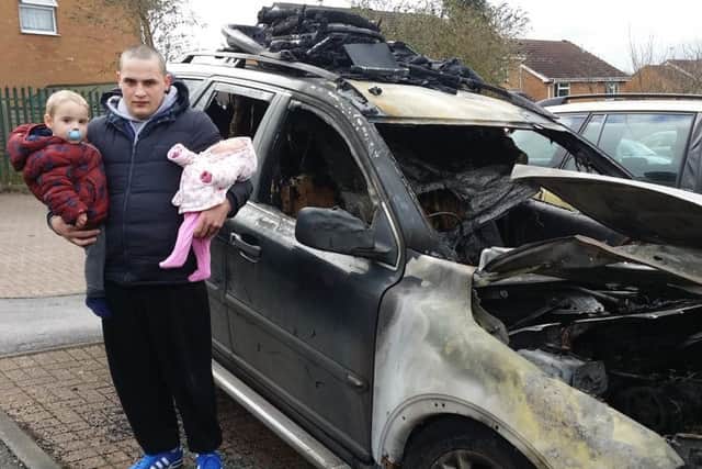James Nairn, holding two of his young children, next to his car which was destroyed in an arson attack in Drummond Walk, Melton EMN-190907-175603001