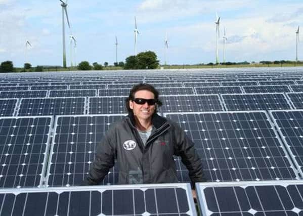 Ecotricity founder Dale Vince in the middle of a field of solar panels with wind turbines in the distance EMN-160216-185747001