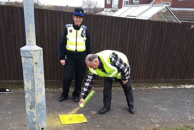 Melton resident and dog patrol volunteer Frank Duckworth highlights a dog fouling hotspot in the Grange Drive area using his temporary spray paint and stencil, watched by a Melton police officer EMN-160329-174546001 EMN-160329-174546001