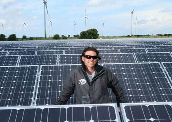 Ecotricity founder Dale Vince in the middle of a field of solar panels with wind turbines in the distance EMN-160524-090651001